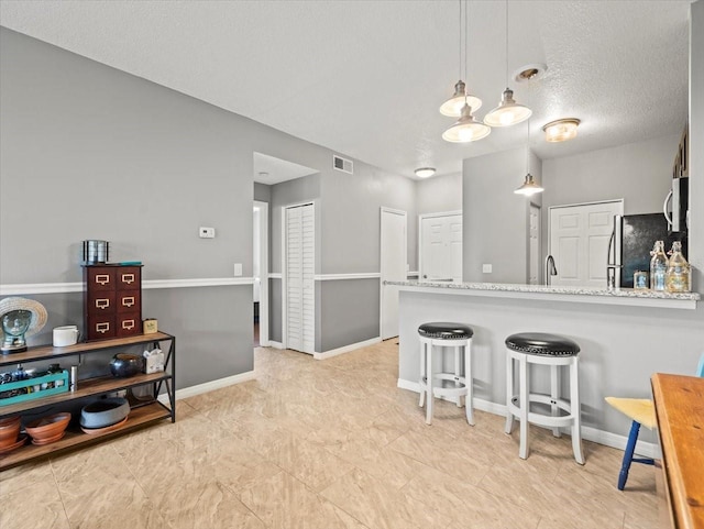 kitchen featuring a textured ceiling, pendant lighting, appliances with stainless steel finishes, a kitchen bar, and kitchen peninsula