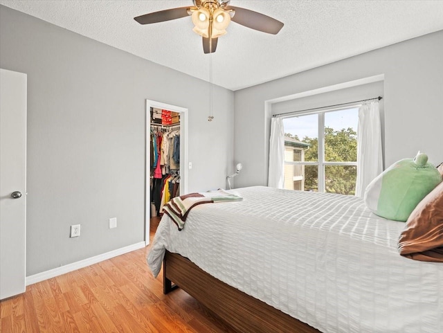 bedroom featuring a textured ceiling, light hardwood / wood-style flooring, ceiling fan, a closet, and a walk in closet