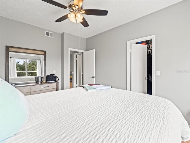 bedroom with a textured ceiling, a walk in closet, ceiling fan, and a closet