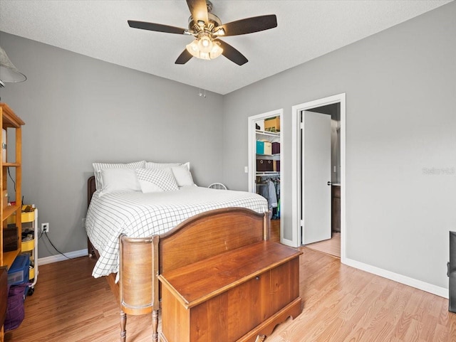 bedroom featuring light wood-type flooring, a walk in closet, a closet, ceiling fan, and a textured ceiling