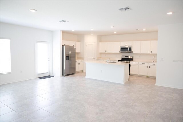 kitchen featuring appliances with stainless steel finishes, sink, light tile patterned floors, white cabinetry, and an island with sink