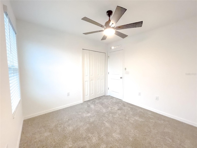 unfurnished bedroom with carpet flooring, ceiling fan, a closet, and multiple windows