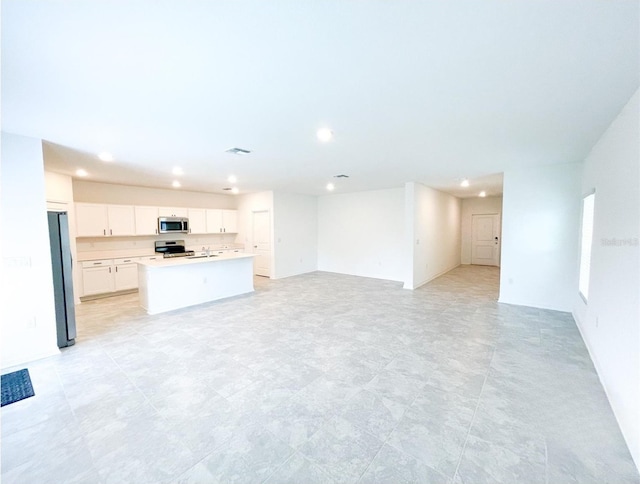 kitchen with open floor plan, an island with sink, light countertops, appliances with stainless steel finishes, and white cabinets