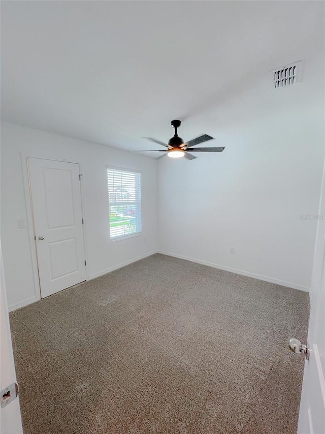 carpeted empty room with visible vents, baseboards, and a ceiling fan