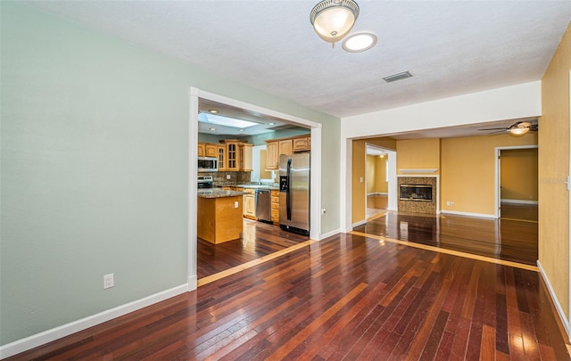 unfurnished living room with a textured ceiling, ceiling fan, and dark hardwood / wood-style flooring