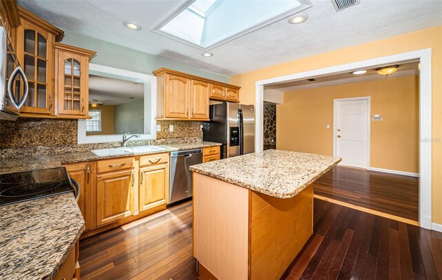 kitchen with a skylight, sink, a kitchen island, stainless steel appliances, and dark hardwood / wood-style flooring