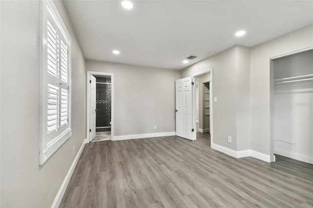 unfurnished bedroom with ensuite bath, a closet, and wood-type flooring