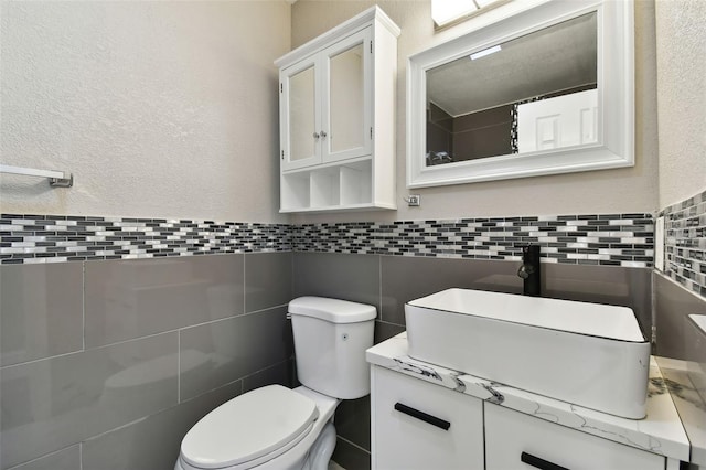 bathroom featuring vanity, toilet, backsplash, and tile walls