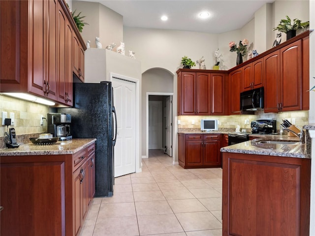 kitchen featuring tasteful backsplash, light tile patterned flooring, arched walkways, black appliances, and a sink