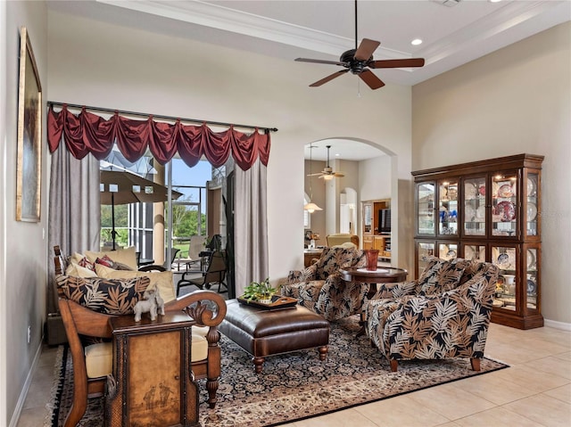 living area featuring tile patterned floors, baseboards, a high ceiling, arched walkways, and a ceiling fan