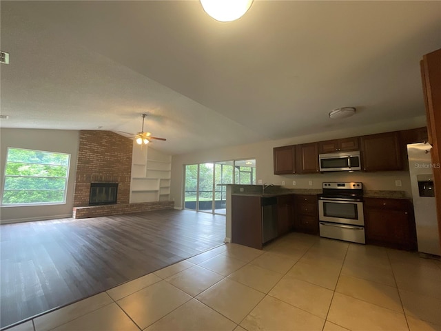 kitchen featuring ceiling fan, lofted ceiling, a brick fireplace, light hardwood / wood-style flooring, and appliances with stainless steel finishes