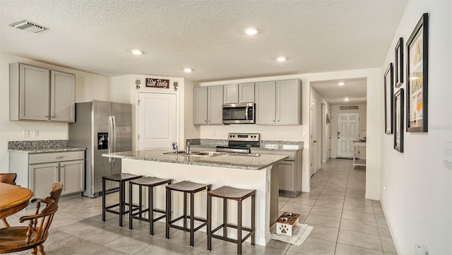 kitchen with gray cabinets, a textured ceiling, a kitchen bar, appliances with stainless steel finishes, and a center island with sink