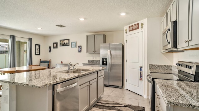 kitchen featuring a textured ceiling, stainless steel appliances, sink, and a center island with sink