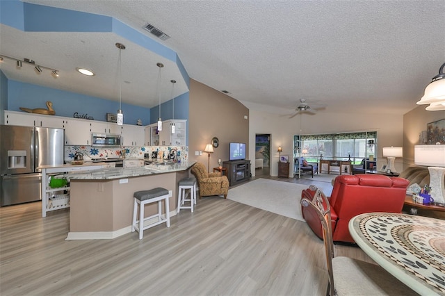 interior space with hanging light fixtures, stainless steel appliances, light hardwood / wood-style flooring, kitchen peninsula, and a textured ceiling