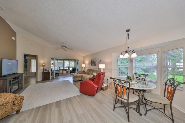 dining space featuring ceiling fan with notable chandelier, a textured ceiling, light wood-type flooring, and lofted ceiling