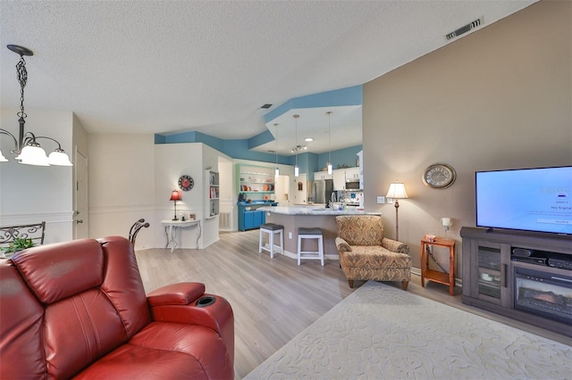 living room with light hardwood / wood-style floors, a textured ceiling, and a notable chandelier