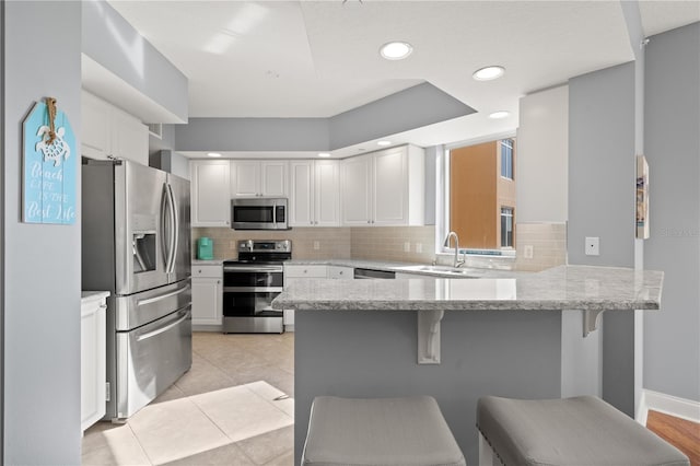 kitchen with white cabinetry, light tile patterned floors, stainless steel appliances, kitchen peninsula, and a breakfast bar area