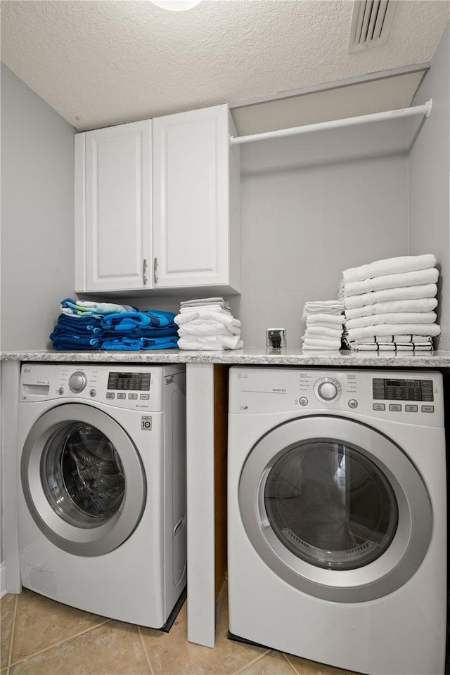 washroom featuring a textured ceiling, cabinets, washer and clothes dryer, and light tile patterned floors