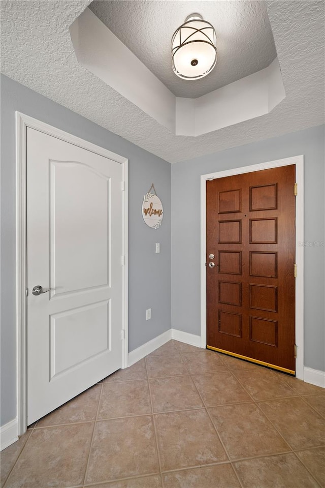 foyer entrance with a textured ceiling, a raised ceiling, and light tile patterned floors