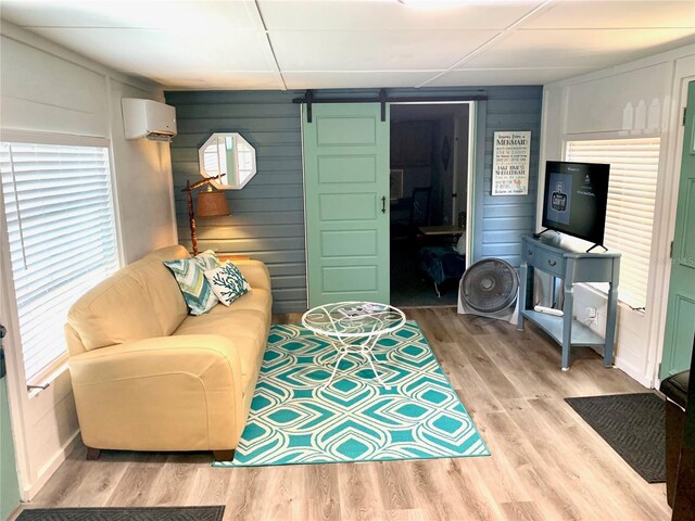 living room featuring a barn door, wood walls, light hardwood / wood-style flooring, and a wall unit AC