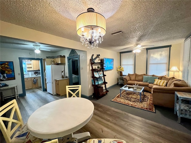 living room with ceiling fan with notable chandelier, a textured ceiling, and wood-type flooring