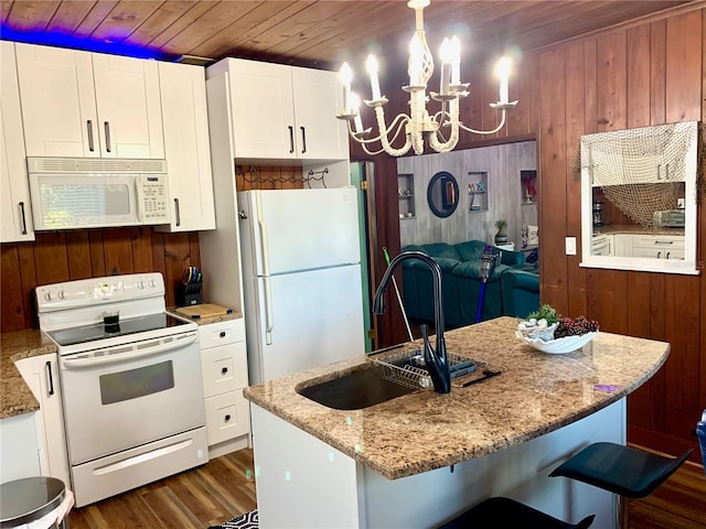 kitchen with dark hardwood / wood-style floors, white appliances, a chandelier, wooden walls, and white cabinets