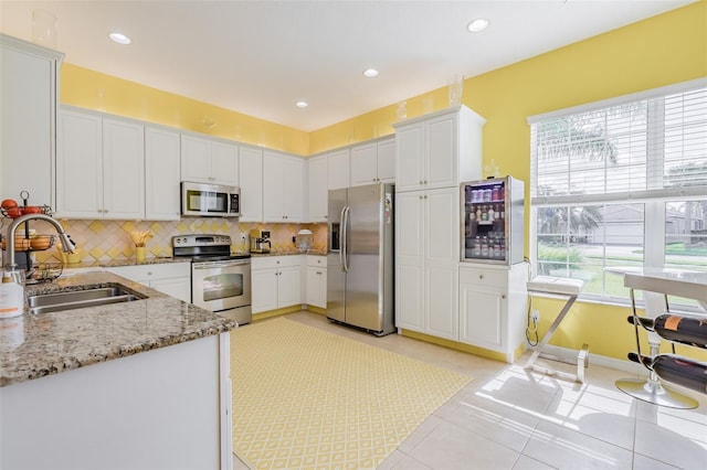 kitchen with light tile patterned floors, stainless steel appliances, sink, light stone counters, and white cabinets