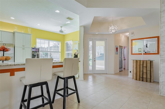 kitchen featuring ceiling fan with notable chandelier, light stone countertops, stainless steel refrigerator, a raised ceiling, and a breakfast bar