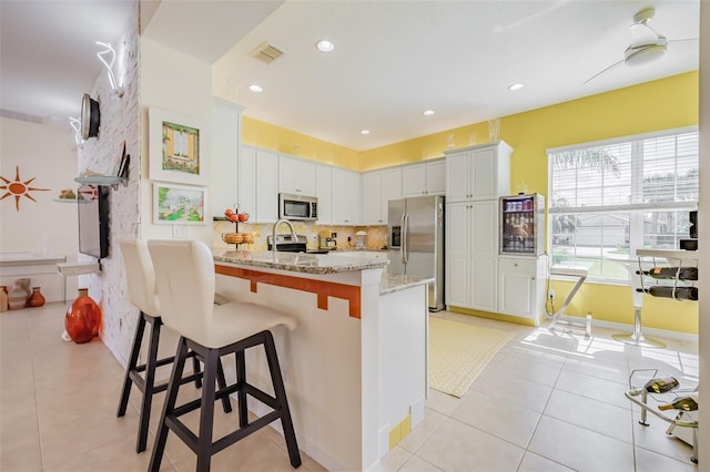 kitchen with stainless steel appliances, white cabinetry, ceiling fan, light stone counters, and light tile patterned flooring