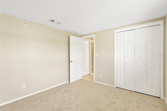 unfurnished bedroom with light carpet, a textured ceiling, and a closet