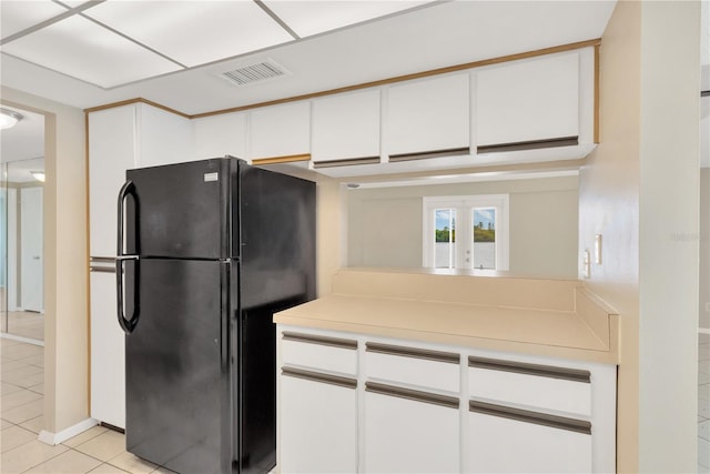 kitchen with light tile patterned floors, black fridge, and white cabinets