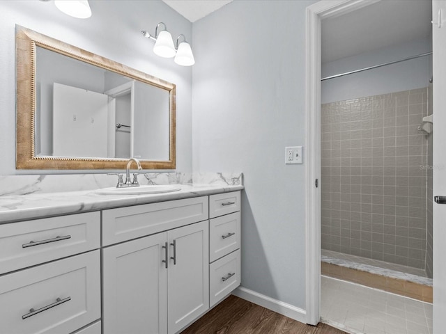 bathroom with wood-type flooring, a tile shower, and vanity