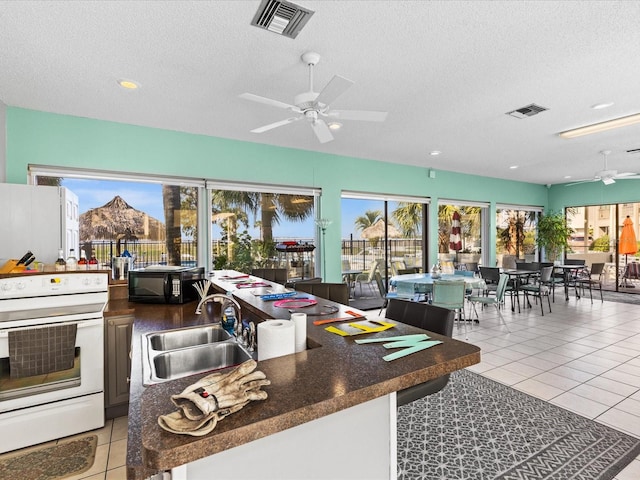 kitchen with a textured ceiling, light tile patterned floors, sink, electric range, and ceiling fan