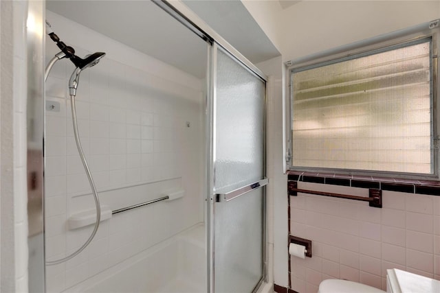 bathroom with tile walls, a shower with shower door, and toilet