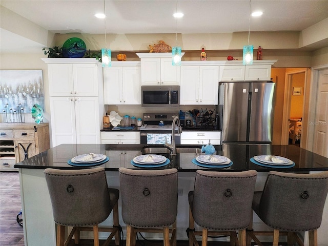 kitchen with white cabinets, hanging light fixtures, appliances with stainless steel finishes, a kitchen island with sink, and dark hardwood / wood-style floors