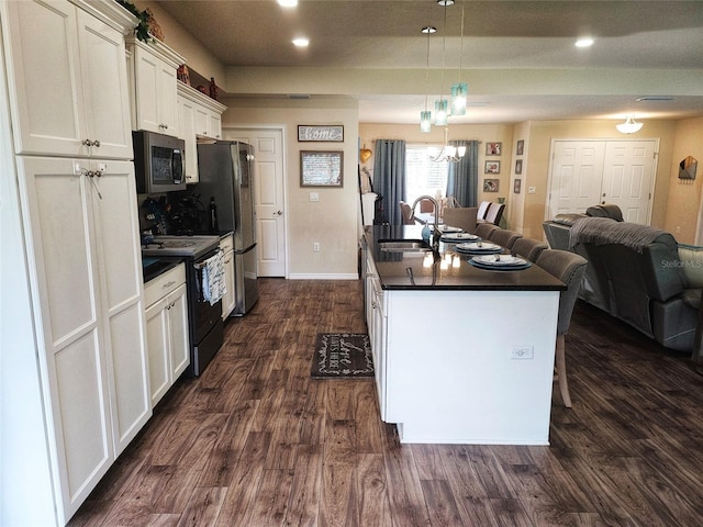 kitchen with a center island with sink, dark hardwood / wood-style flooring, appliances with stainless steel finishes, sink, and decorative light fixtures