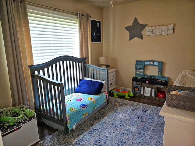 bedroom with a crib and dark wood-type flooring