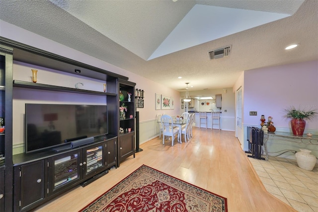 living room with vaulted ceiling, light wood-style floors, visible vents, and a textured ceiling