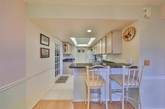 kitchen featuring dark countertops, a kitchen breakfast bar, a peninsula, white appliances, and a sink