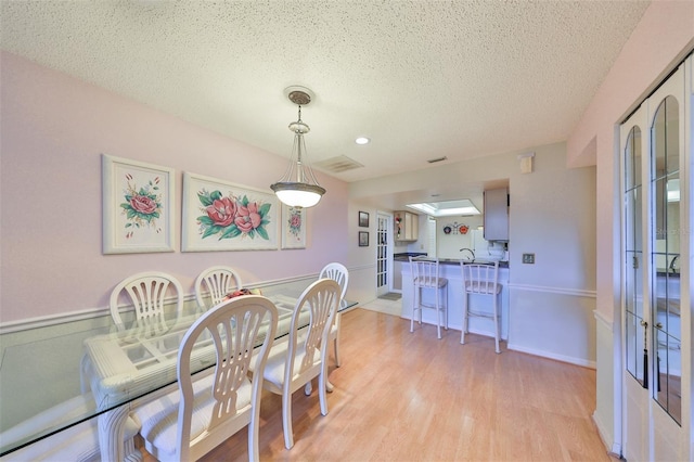 dining area with visible vents, baseboards, a textured ceiling, and light wood-style flooring