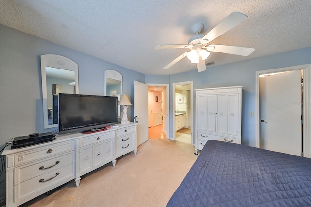 bedroom with a textured ceiling, light colored carpet, ceiling fan, and ensuite bath