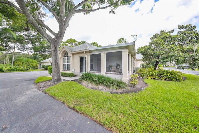 view of front of property with stucco siding, a front yard, and a sunroom