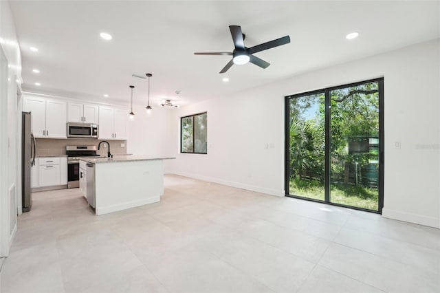 kitchen featuring decorative light fixtures, light stone countertops, stainless steel appliances, ceiling fan, and a kitchen island with sink