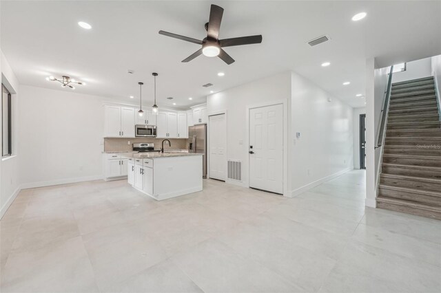 kitchen with a kitchen island with sink, white cabinetry, decorative light fixtures, stainless steel appliances, and ceiling fan