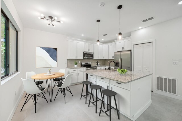 kitchen with an island with sink, appliances with stainless steel finishes, white cabinets, and tasteful backsplash