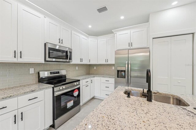 kitchen with appliances with stainless steel finishes, white cabinetry, sink, and tasteful backsplash