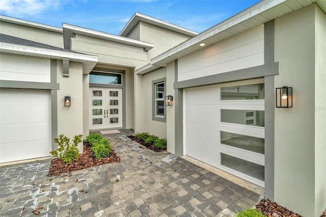 view of exterior entry featuring decorative driveway, an attached garage, and stucco siding