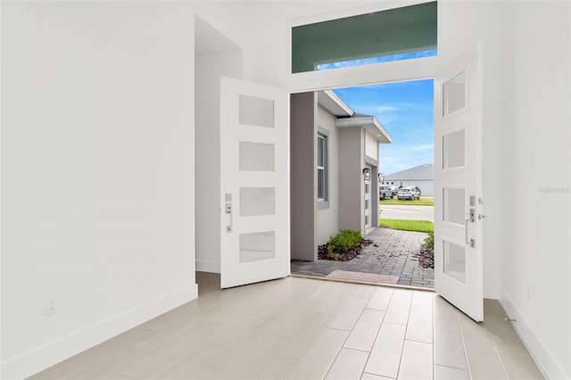 foyer with light wood-style floors, french doors, a wall of windows, and baseboards