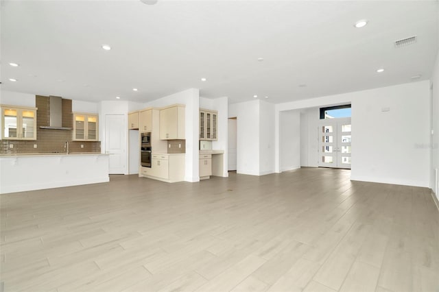 unfurnished living room with visible vents, light wood-type flooring, recessed lighting, french doors, and a sink