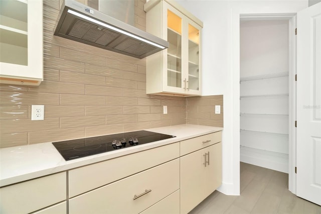 kitchen with tasteful backsplash, ventilation hood, light countertops, glass insert cabinets, and black electric stovetop